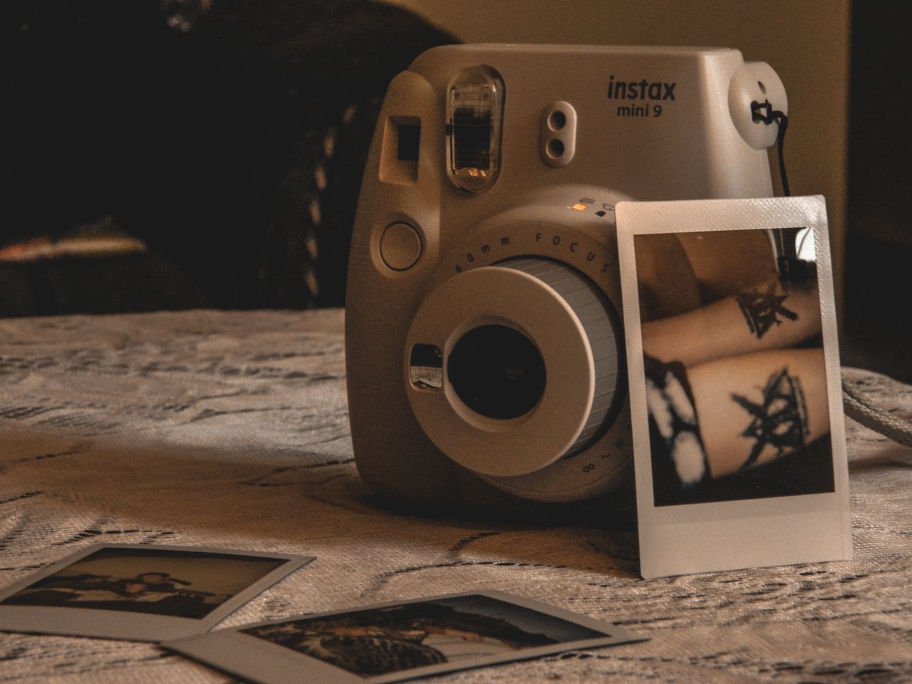 Close-up of an Instax Mini 9 camera with polaroid photos on a textured surface.