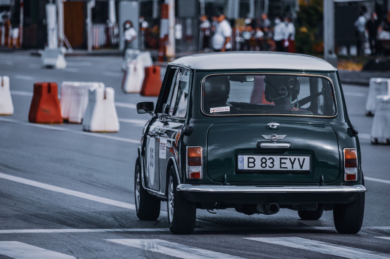 Anonymous people driving vintage automobile with numbers on blurred background of crowd in district of town